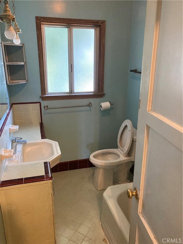 bathroom featuring tile patterned flooring, vanity, baseboards, a bathing tub, and toilet