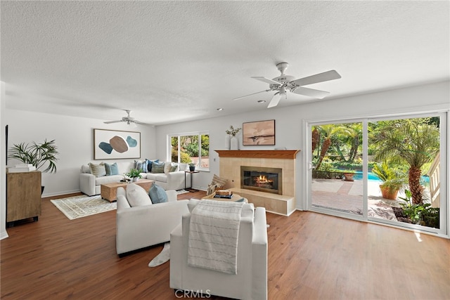 living room with a tile fireplace, a textured ceiling, wood finished floors, and ceiling fan