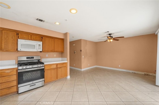 kitchen featuring stainless steel gas range, tile countertops, a ceiling fan, white microwave, and visible vents
