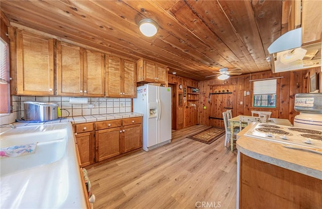 kitchen with brown cabinetry, white refrigerator with ice dispenser, wood ceiling, a ceiling fan, and light wood finished floors