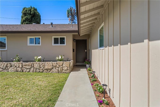 property entrance featuring a lawn, a shingled roof, and board and batten siding