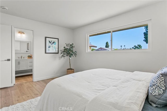 bedroom featuring baseboards, a sink, light wood-style flooring, and ensuite bathroom