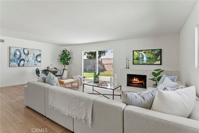 living room with a brick fireplace, baseboards, visible vents, and light wood finished floors