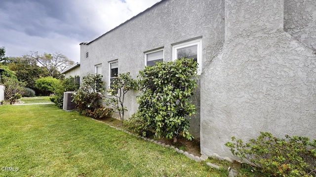 view of side of home featuring central AC unit, stucco siding, and a yard