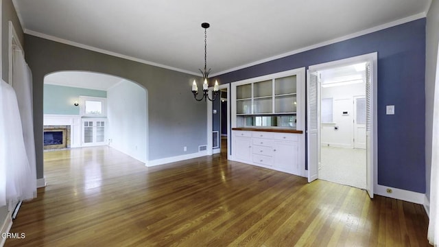 unfurnished dining area with arched walkways, baseboards, dark wood-style floors, and a notable chandelier