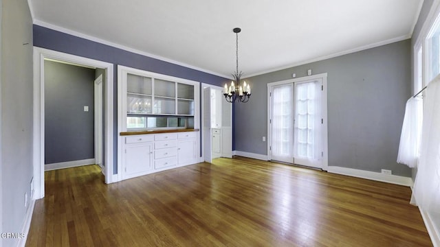 unfurnished dining area featuring dark wood-type flooring, ornamental molding, plenty of natural light, and a notable chandelier