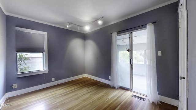 empty room with visible vents, ornamental molding, track lighting, wood finished floors, and baseboards