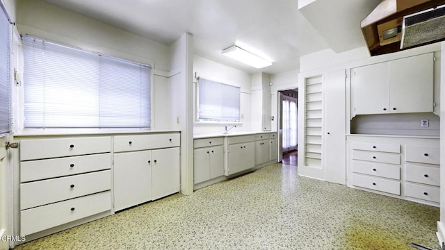 kitchen featuring light countertops, white cabinetry, a sink, and light speckled floor