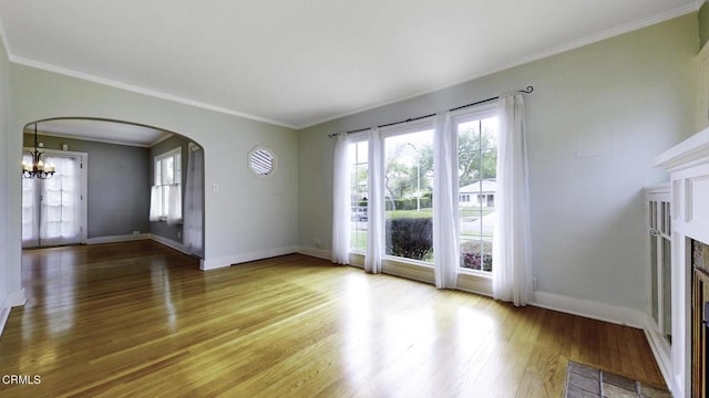 unfurnished living room featuring crown molding, arched walkways, baseboards, and wood finished floors