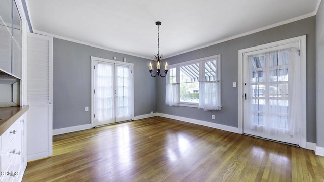 unfurnished dining area with baseboards, an inviting chandelier, ornamental molding, and wood finished floors