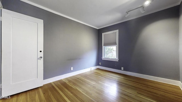 empty room with crown molding, baseboards, track lighting, and wood finished floors