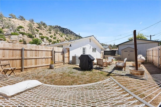 view of yard featuring a storage shed, central AC unit, a gate, a fenced backyard, and a patio