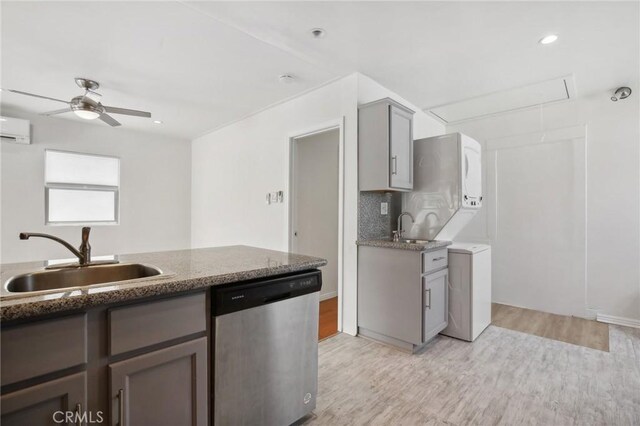 kitchen with gray cabinets, dishwasher, a sink, light wood finished floors, and stacked washer and clothes dryer