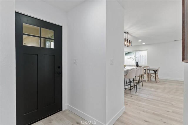 foyer with light wood-style floors, baseboards, and an inviting chandelier