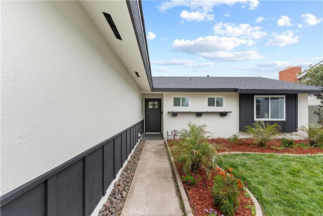 entrance to property with stucco siding, a yard, and a chimney