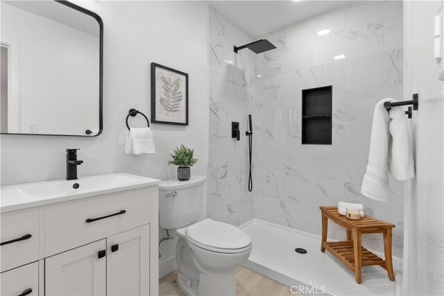 bathroom with wood finished floors, toilet, a marble finish shower, and vanity