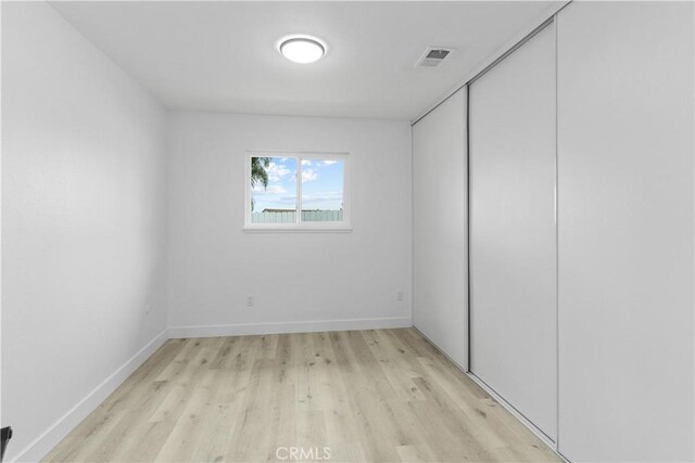unfurnished bedroom with baseboards, a closet, light wood-style flooring, and visible vents