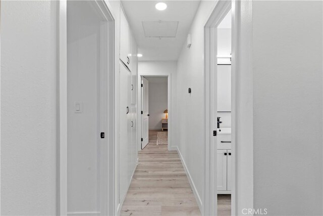hallway with baseboards, attic access, and light wood-style flooring