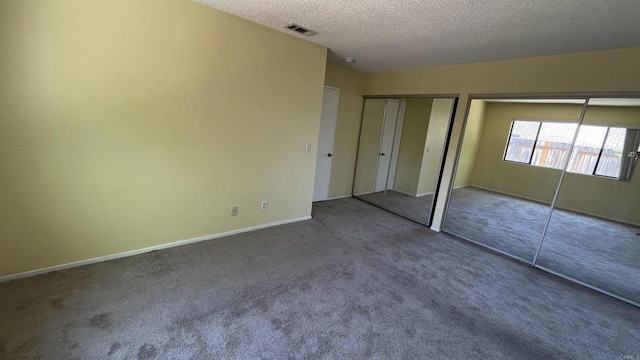 unfurnished bedroom featuring carpet flooring, a textured ceiling, two closets, baseboards, and visible vents