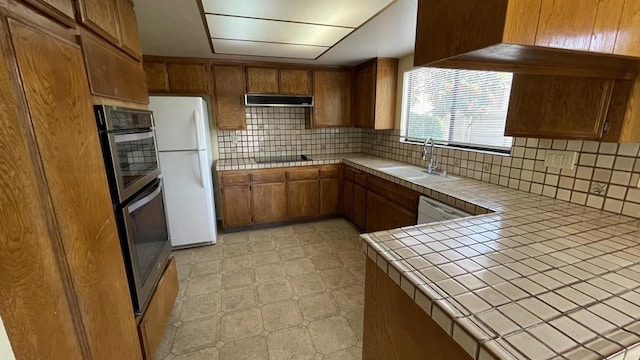 kitchen with a sink, tile countertops, brown cabinets, and freestanding refrigerator