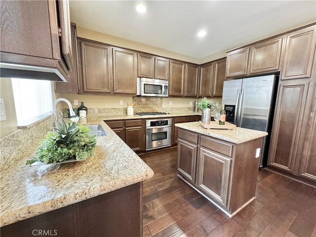 kitchen with a kitchen island, appliances with stainless steel finishes, a sink, light stone counters, and recessed lighting