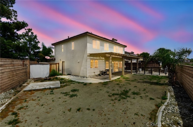 back of property at dusk with a fenced backyard, a patio, and stucco siding