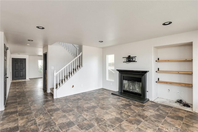 unfurnished living room featuring plenty of natural light, baseboards, a glass covered fireplace, and stairway