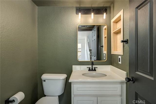 bathroom featuring vanity, a textured wall, and toilet