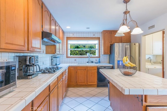 22437 Haynes St, West Hills, CA 91307 - kitchen featuring tile countertops, washing machine and dryer, under cabinet range hood, visible vents, and appliances with stainless steel finishes