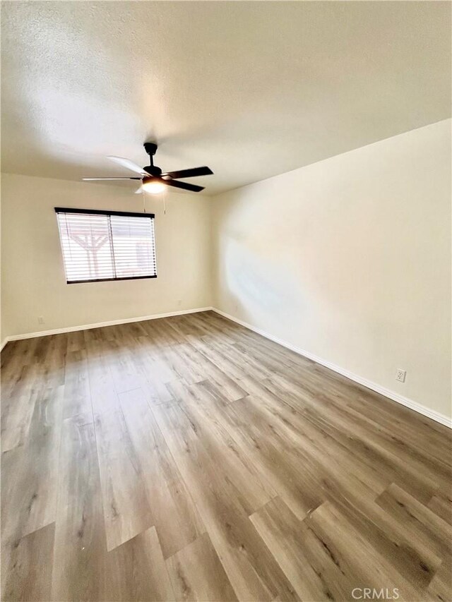 unfurnished room with baseboards, ceiling fan, a textured ceiling, and wood finished floors