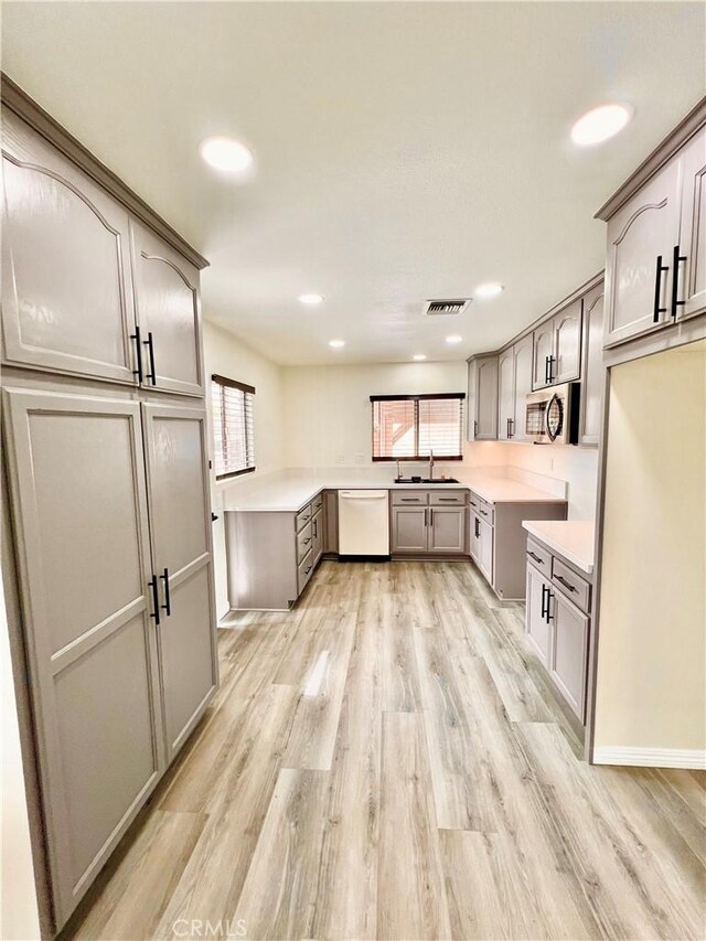 kitchen featuring white dishwasher, stainless steel microwave, a healthy amount of sunlight, and light wood finished floors