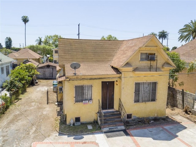 view of front of house with a shingled roof, stucco siding, entry steps, and fence