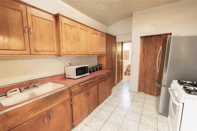 kitchen with a sink, white appliances, brown cabinetry, light tile patterned floors, and vaulted ceiling