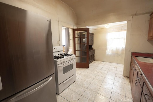 kitchen featuring freestanding refrigerator, white gas stove, a sink, light tile patterned floors, and vaulted ceiling