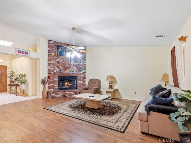 18668 Kamana Rd, Apple Valley, CA 92307 - living room featuring a ceiling fan, visible vents, vaulted ceiling, a brick fireplace, and wood finished floors