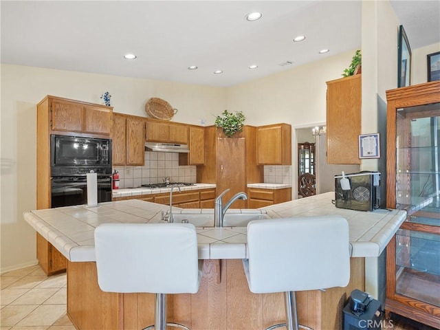 18668 Kamana Rd, Apple Valley, CA 92307 - kitchen with tile counters, under cabinet range hood, black appliances, and tasteful backsplash