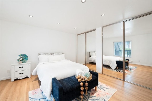 bedroom with two closets, recessed lighting, and light wood-style flooring