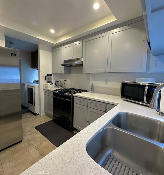 kitchen with a tray ceiling, a sink, light countertops, under cabinet range hood, and stainless steel appliances