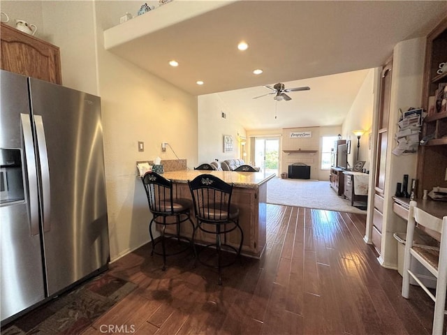 kitchen featuring stainless steel fridge with ice dispenser, ceiling fan, a fireplace, and dark wood-style floors