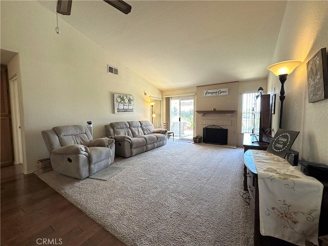 living area with ceiling fan, a fireplace, wood finished floors, lofted ceiling, and visible vents