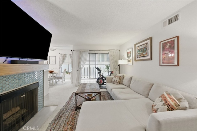 carpeted living area featuring a textured ceiling, visible vents, and a tile fireplace