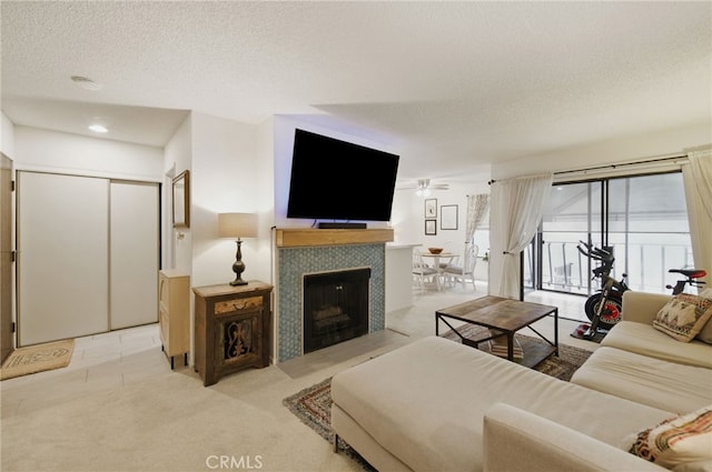 living room featuring a tiled fireplace, a ceiling fan, a textured ceiling, and light colored carpet