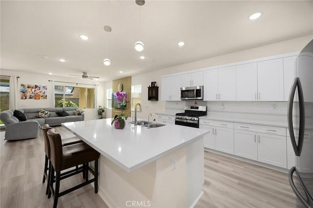 kitchen featuring ceiling fan, a sink, white cabinets, light wood finished floors, and stainless steel appliances