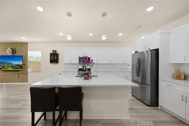 kitchen with white cabinets, tasteful backsplash, light countertops, stainless steel appliances, and light wood-type flooring