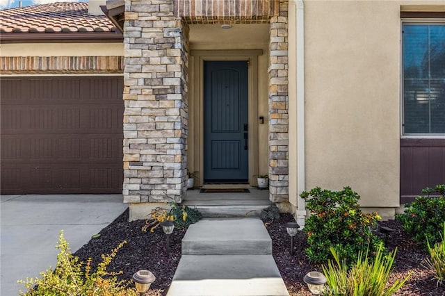 entrance to property with an attached garage, stone siding, and stucco siding
