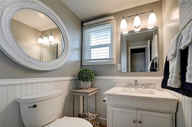 half bathroom with a wainscoted wall, vanity, and toilet