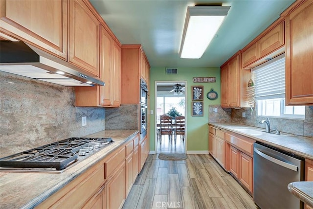 kitchen with appliances with stainless steel finishes, a sink, baseboards, light countertops, and under cabinet range hood