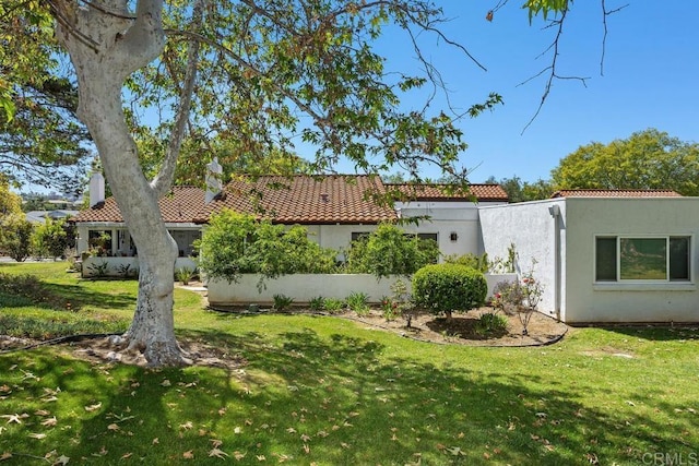 rear view of property featuring a yard, a tile roof, and stucco siding