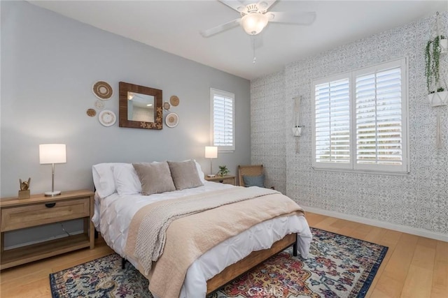 bedroom featuring a ceiling fan, wallpapered walls, baseboards, and hardwood / wood-style floors