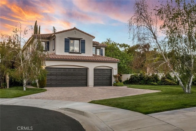 mediterranean / spanish-style home with a tiled roof, driveway, a front yard, an attached garage, and stucco siding